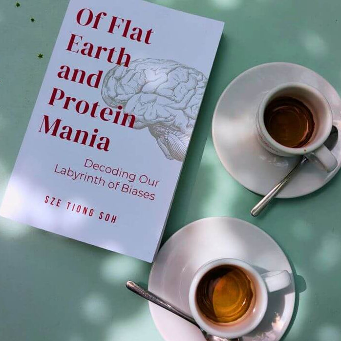 Book titled 'Of Flat Earth and Protein Mania' on a table with two cups of coffee.
